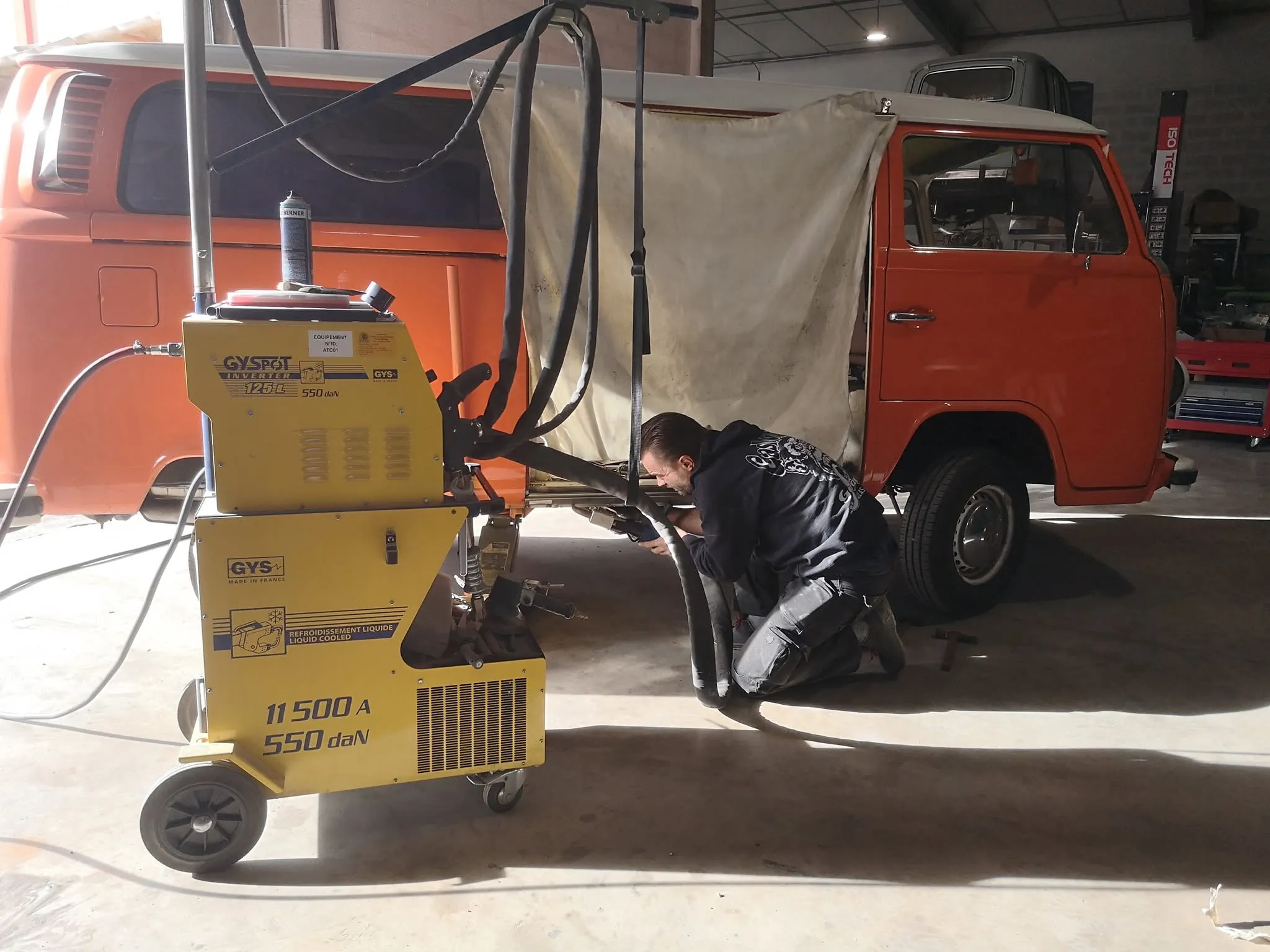 Carrossier intervenant sur le bas de caisse d’un Combi Volkswagen orange dans l’atelier