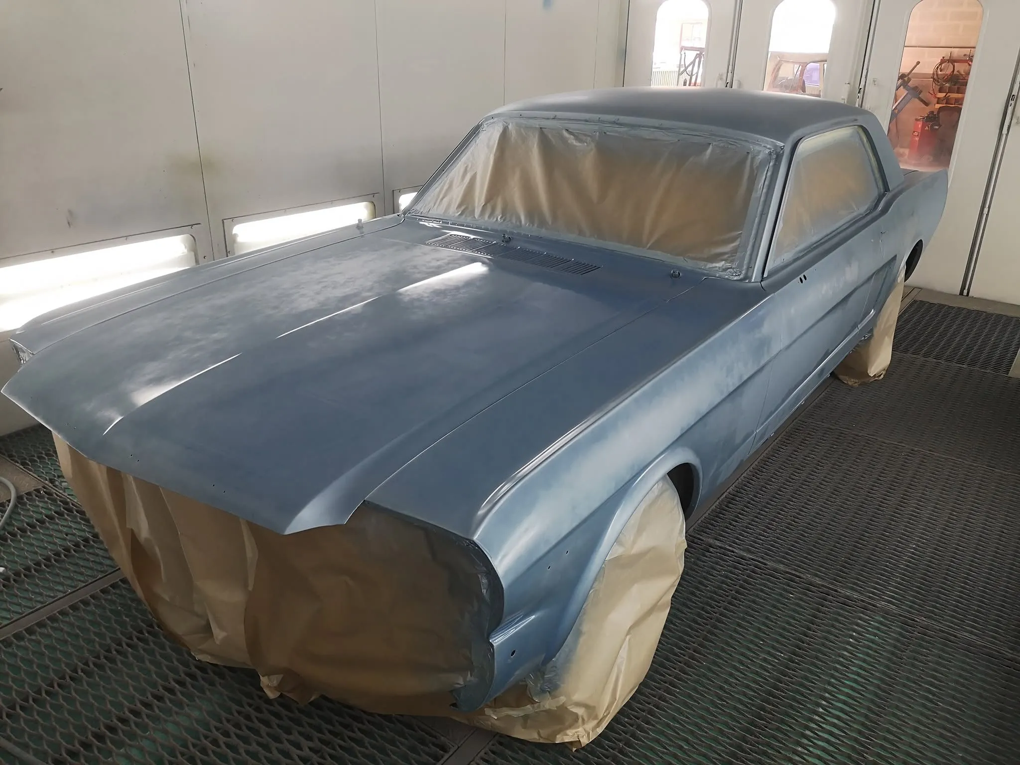 Mustang ancienne bleu clair en apprêt, masquée dans une cabine de peinture
