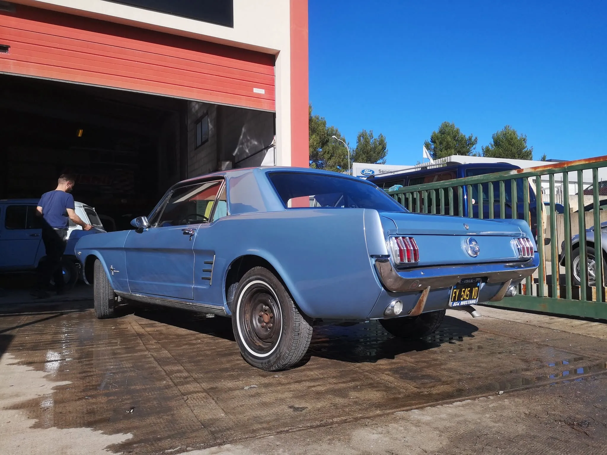 Mustang ancienne bleu clair remontée, vue de trois quarts arrière devant l’atelier