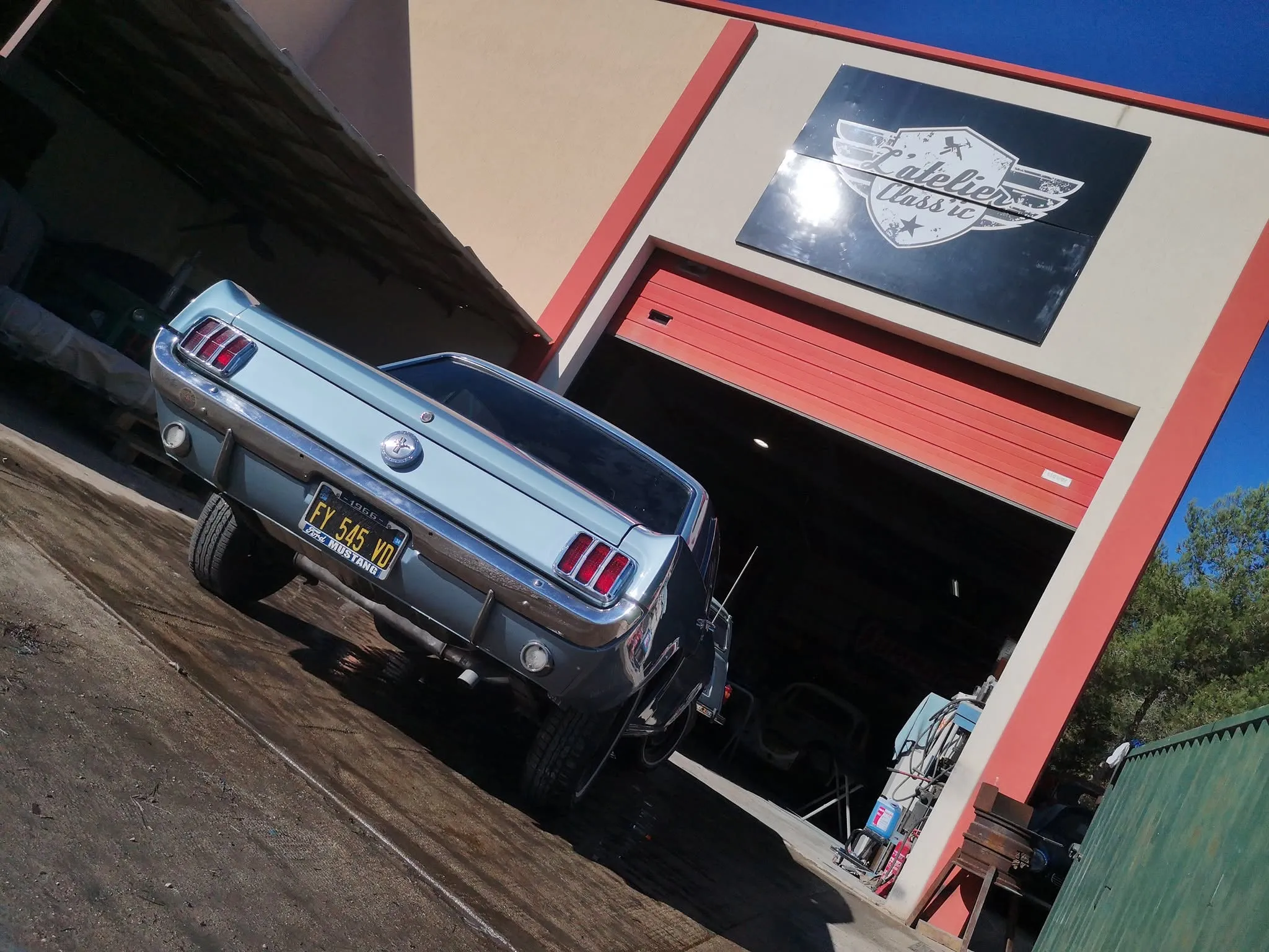 Mustang ancienne bleu clair terminée devant l’enseigne de L'Atelier Class'ic
