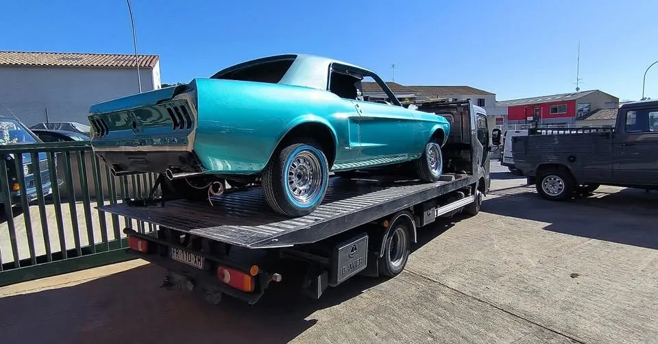 Mustang turquoise partiellement démontée vue de l’arrière sur un camion plateau